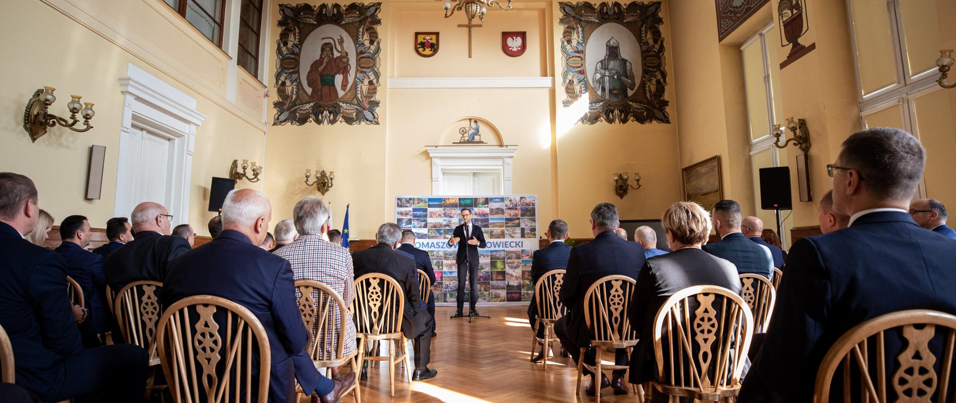 wiceminister Waldemar mówi do mikrofonu, uczestnicy spotkania siedzą na krzesłach