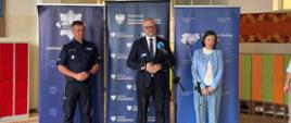 Trzy osoby: Dwóch mężczyzn i kobieta stoją za mikrofonami i czekają na swoje wystąpienie 