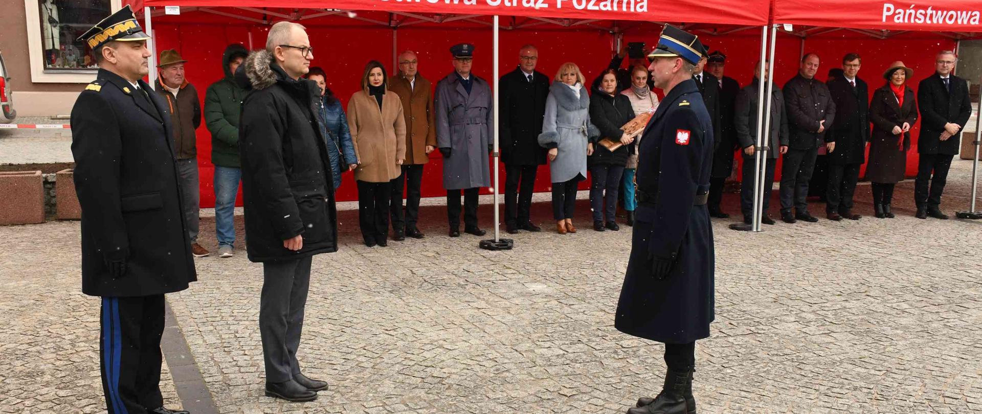 Samorządowcy i strażacy stojący na placu