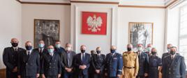 Wojewoda pomorski, przedstawiciele Policji, Państwowej Straży Pożarnej, straży miejskich i gminnych stoją obok siebie. Za nimi wiszą obrazy z marszałkiem Piłsudskim oraz godło Polski - biały orzeł na czerwonym tle.