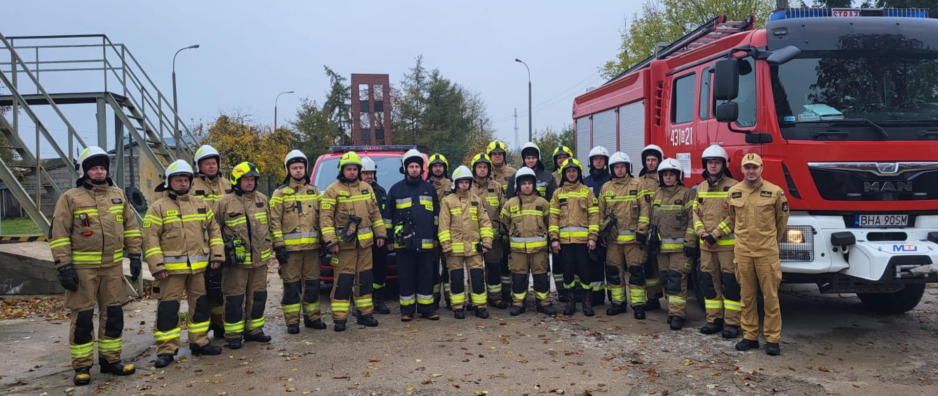 Na placu obok strażackich wozów bojowych w dwóch rzędach stoi kilkudziesięciu strażaków