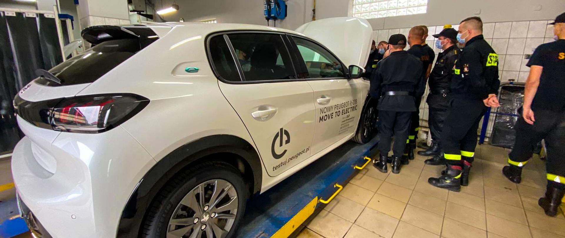 Strażacy obserwują silnik samochodu osobowego.