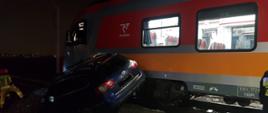 Widać pociąg osobowy, na torowisku jest samochód osobowy