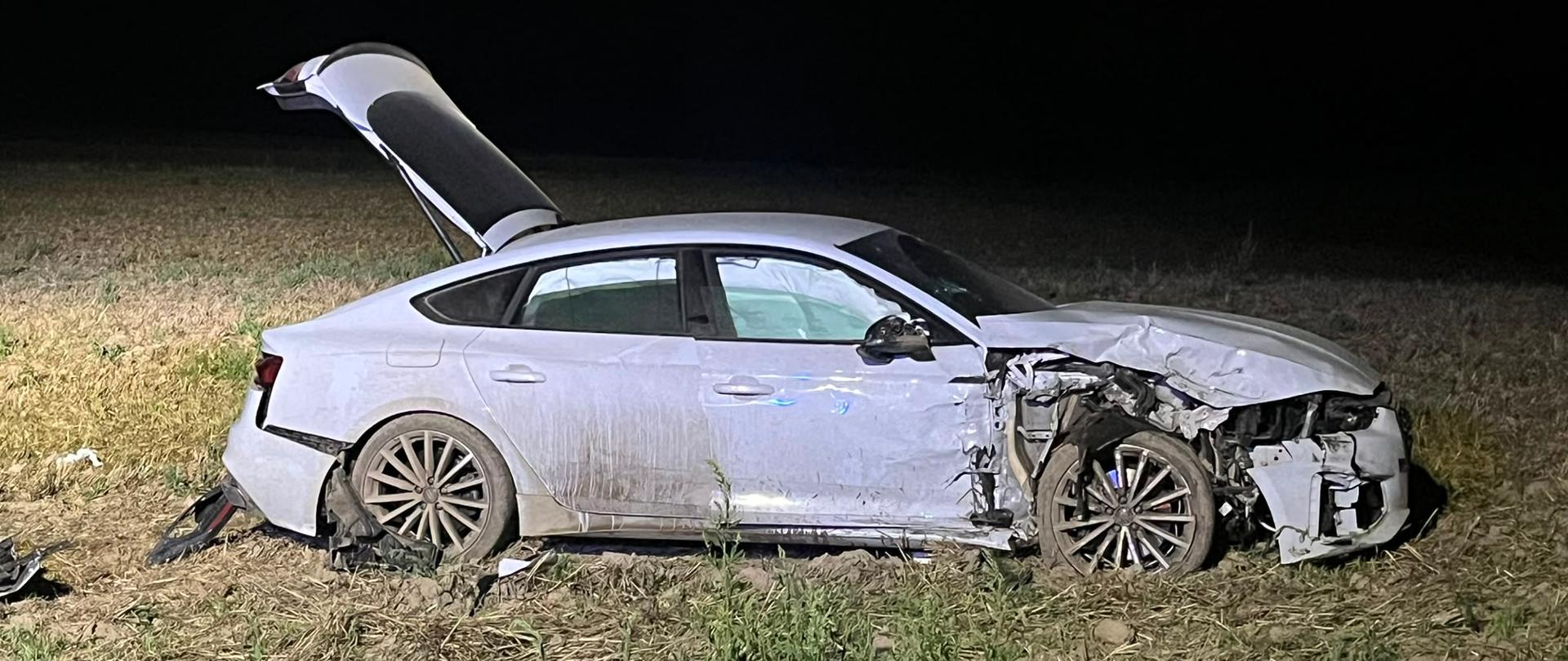 Uszkodzony jasny samochód na polu, jest noc