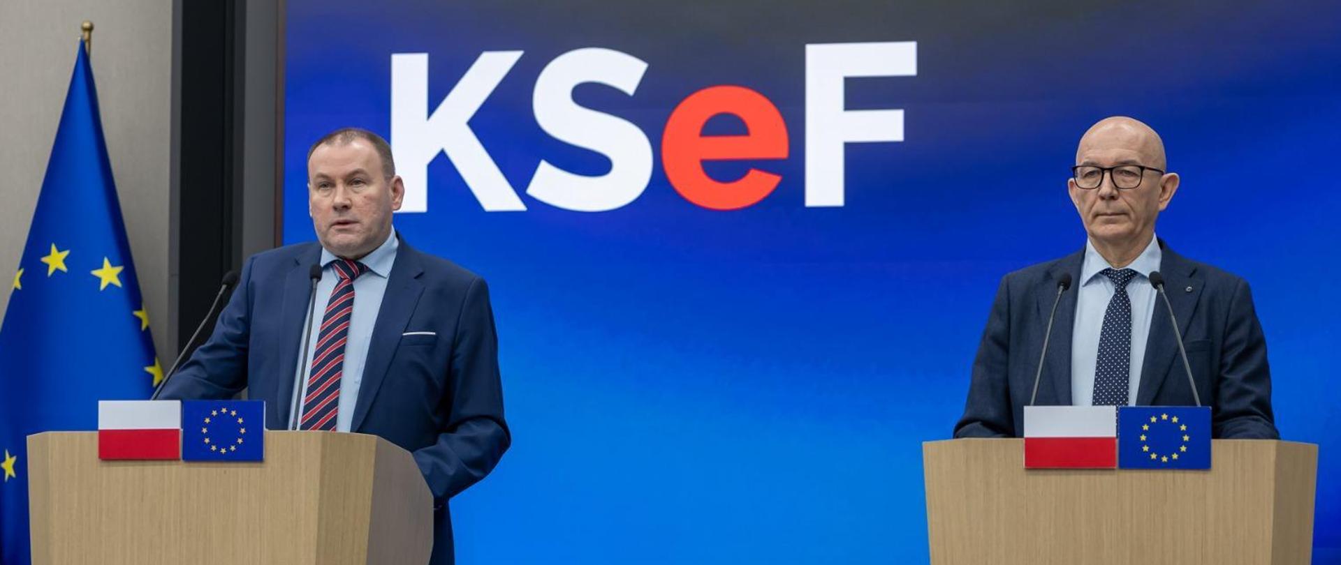 Zbigniew Stawicki, Podsekretarz Stanu w Ministerstwie Finansów, Zastępca Szefa Krajowej Administracji Skarbowej oraz Roman Łożyński, dyrektor Centrum Informatyki Resortu Finansów przy mównicach z flagami Polski i Unii Europejskiej na tle ekranu z logo KSeF