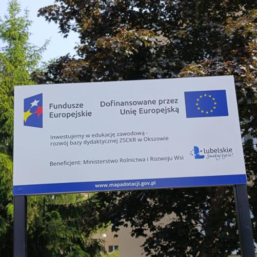 Tablica informacyjna Funduszy Europejskich przy ZSCKR w Okszowie, informująca o dofinansowaniu rozwoju bazy dydaktycznej przez Unię Europejską.