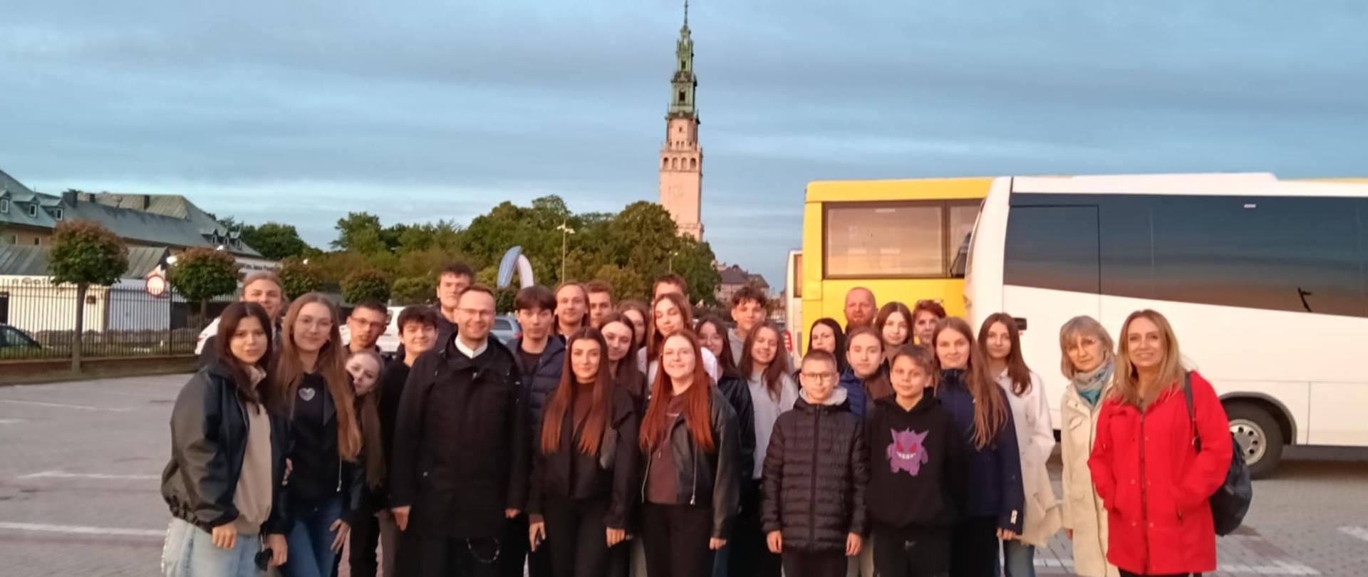 członkowie Kameralnego Chóru Projektowego wraz z opiekunami na parkingu przed autobusem tuż po zakończeniu koncertu ona Jasnej Górze. W tle widoczna jest wieża kościelna.