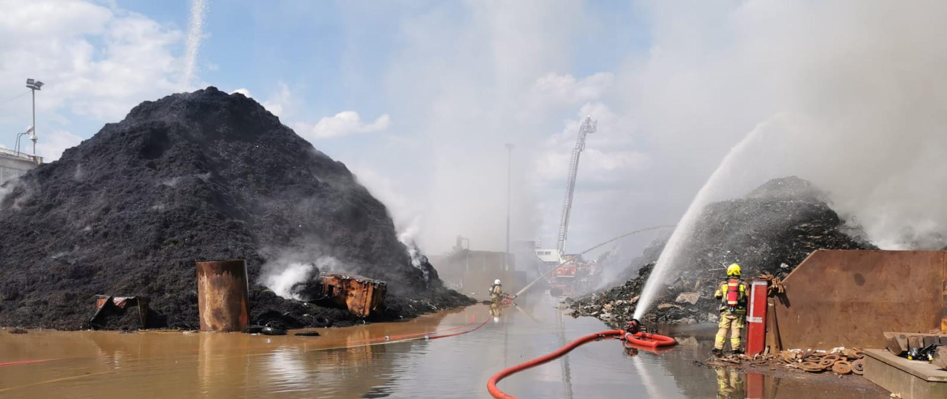 Pożar Przysieka Polska. Na zdjęciu widać hałdy palących się odpadów, wozy strażackie i strażaków gaszących pożar.