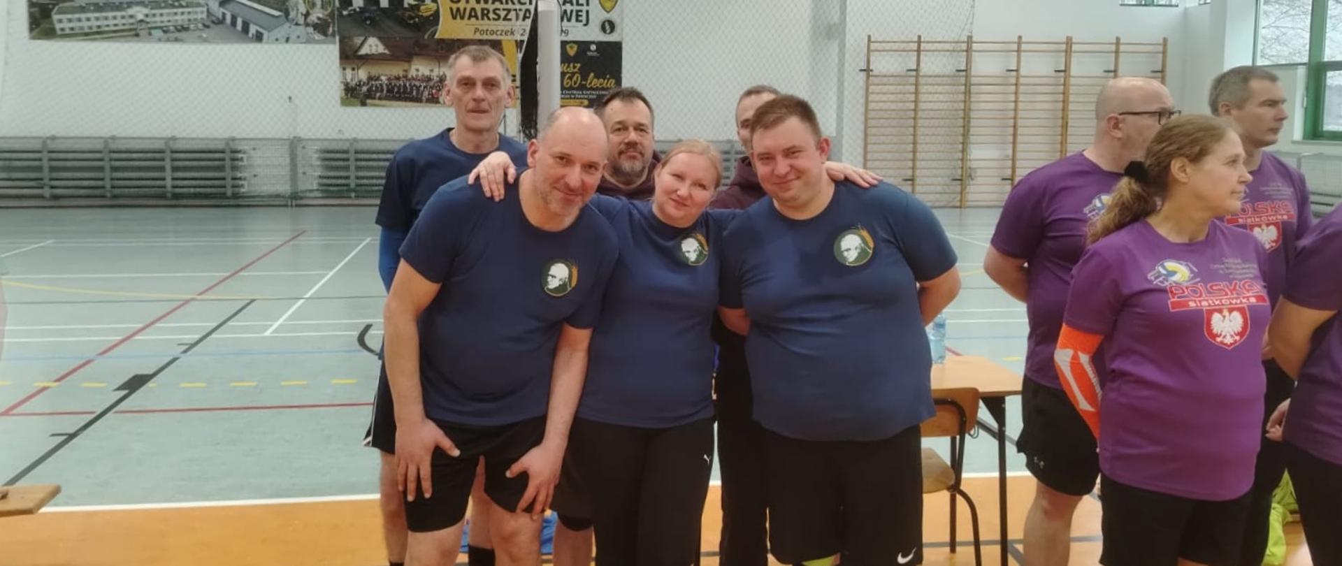 Grupa zawodników w sportowych strojach pozuje do zdjęcia w hali sportowej.