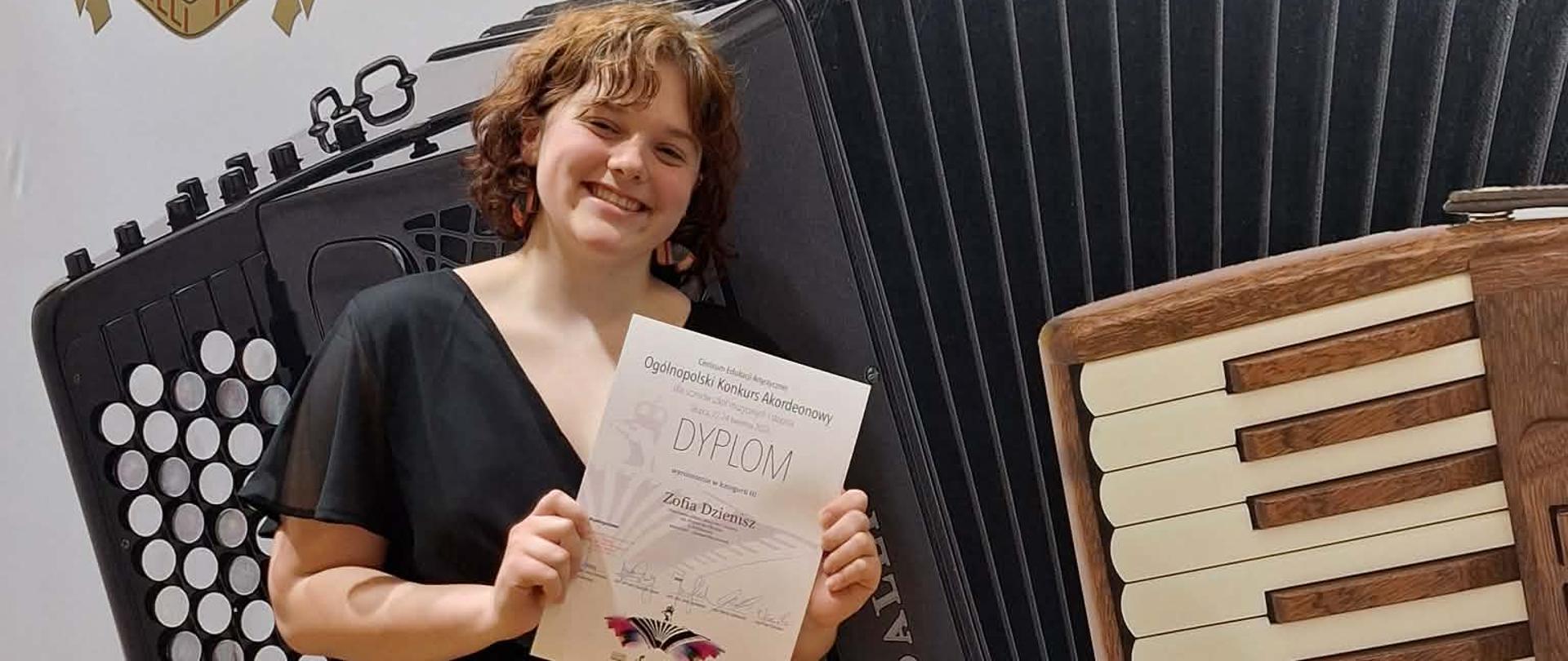 Zofia Dzienisz pozuje na tle logo z akordeonami trzymając dyplom laureata.