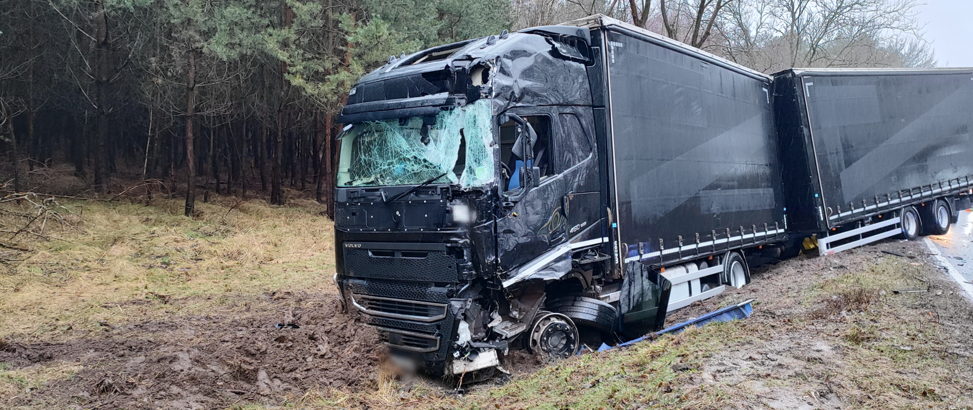 Na zdjęciu widać samochód ciężarowy z rozbitą kabiną, znajdujący się poza pasem jezdni 
