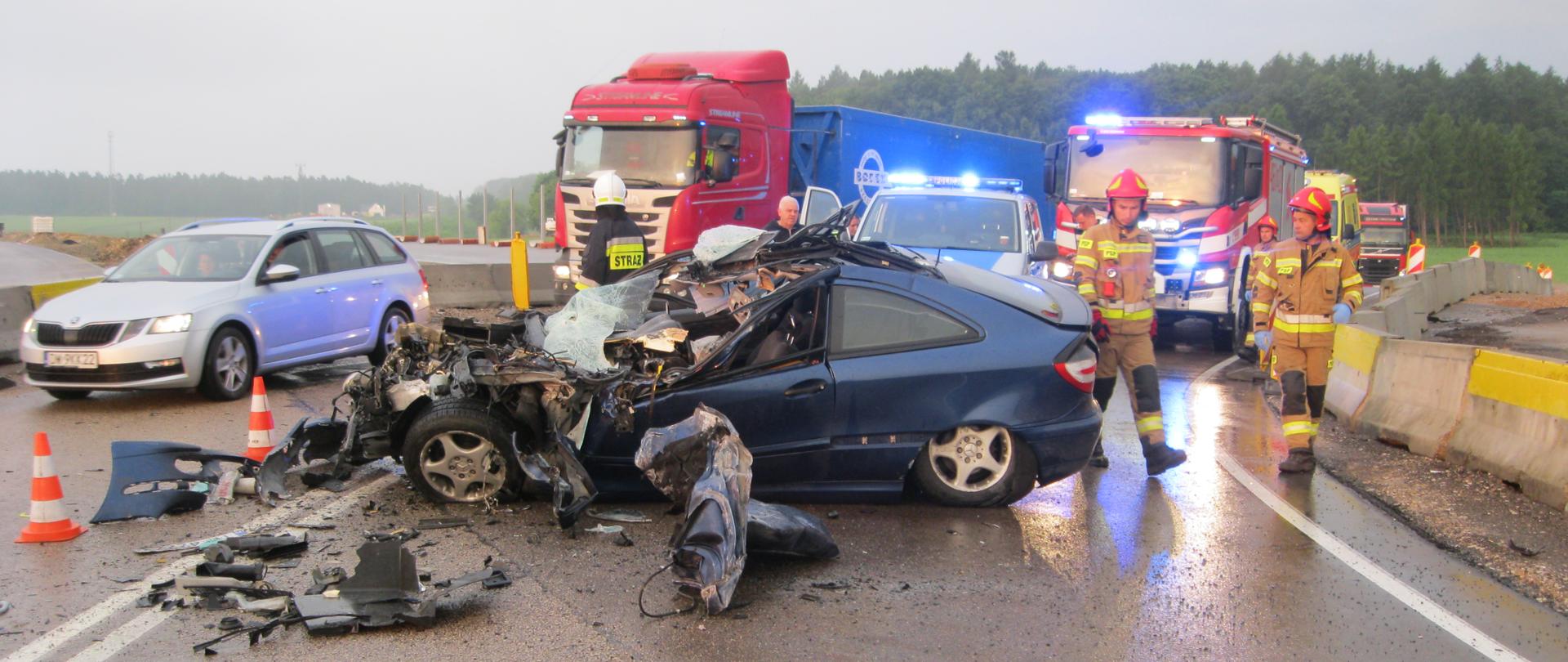 Na zdjęciu widoczny rozbity samochód osobowy, strażacy z tyłu widoczne pojazd pożarniczy oraz karetka ZRM