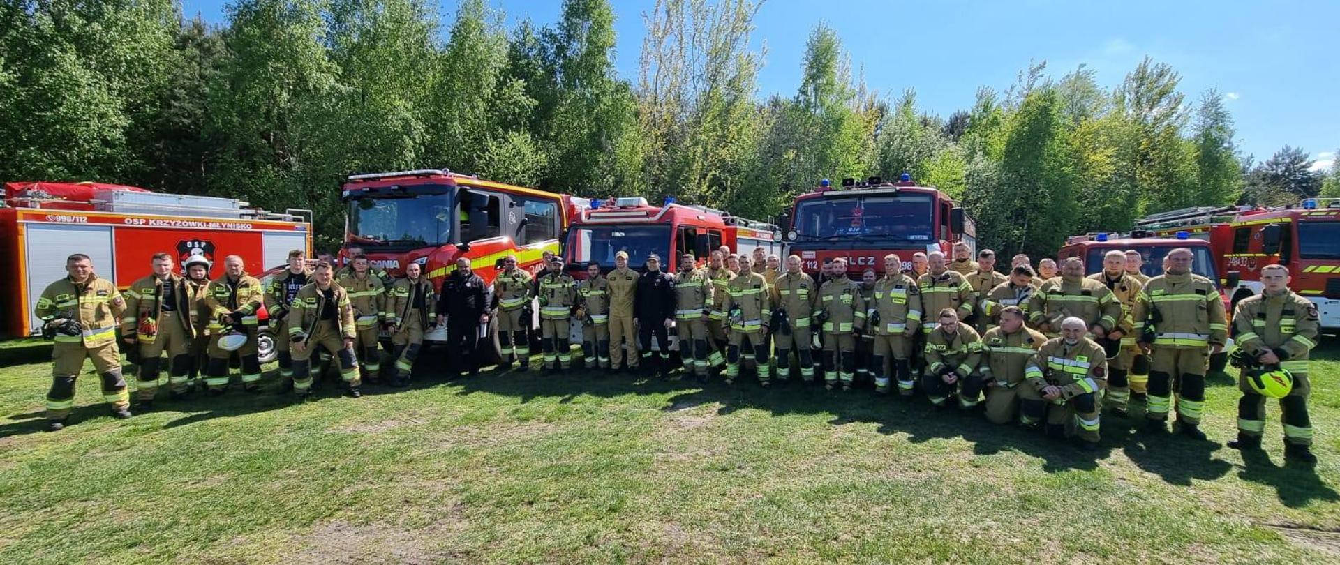 Strażacy na tle samochodów strażackich.