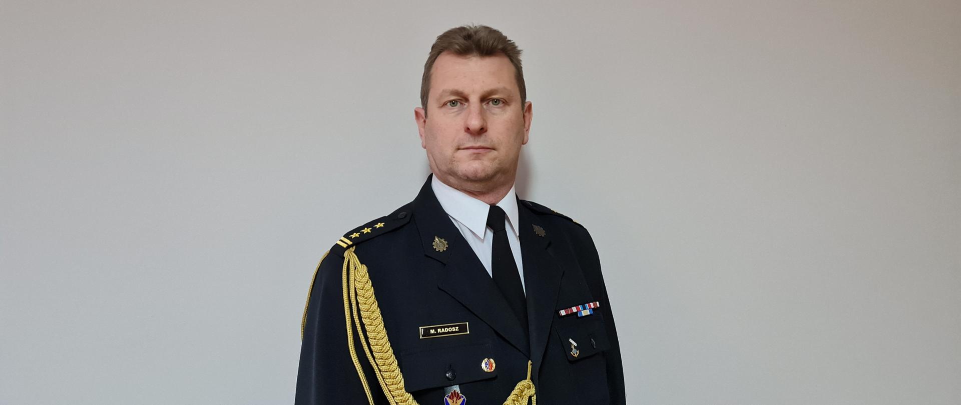 Zdjęcie przedstawia st. bryg. Marka Radosza Komendanta Miejskiego Państwowej Straży Pożarnej w Częstochowie w mundurze galowym na szarym tle. 