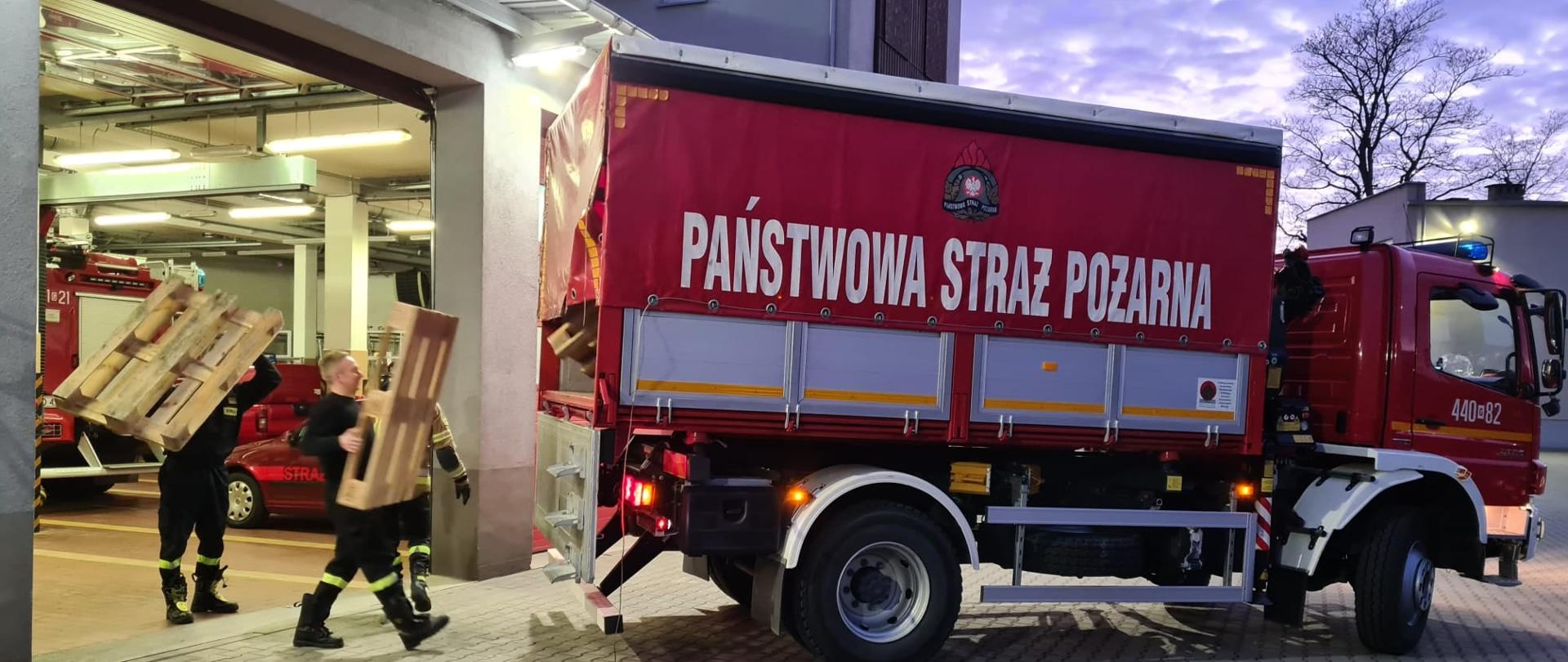 Zdjęcie przedstawia strażaków podczas załadunku sprzętu pożarniczego na samochód ciężarowy Państwowej Straży Pożarnej.