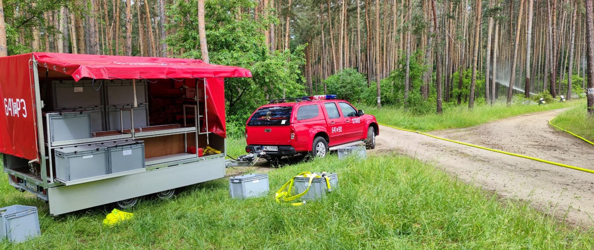 Las, samochód z przyczepą, skrzynie, w tle strażacy podają wodę