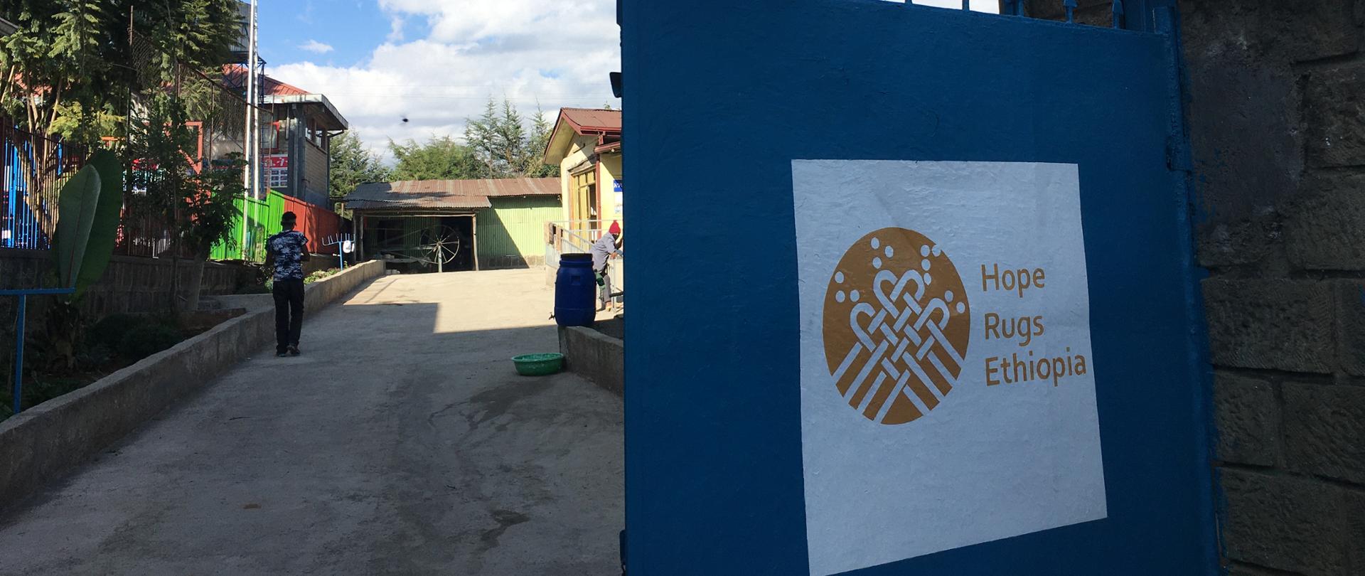  Zaprojektowany w ramach projektu logotyp Hope Rugs Ethiopia na bramie siedziby HBRHA. Autor: Maciej Chrzanowski, 2020.12.14, Addis Abeba,