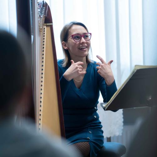 zdjęcie przedstawia wykładowcę przemawiającego i gestykulującego przy harfie w sali kameralnej