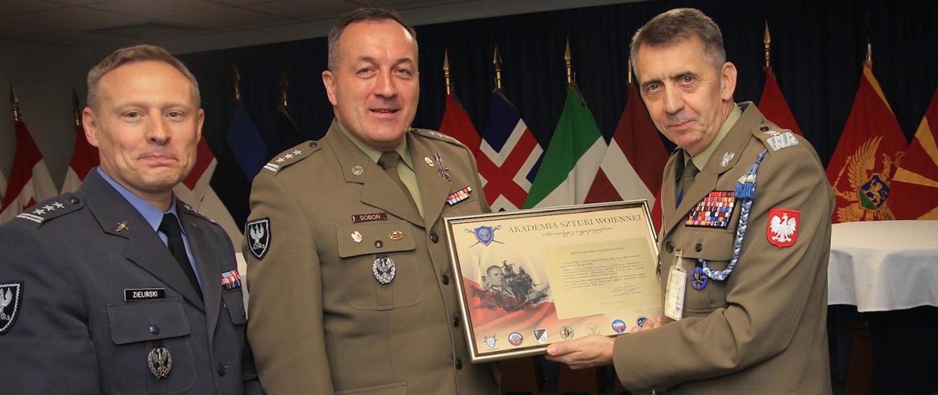 Polscy oficerowie stoją na tle flag NATO. Generał Wojciechowski prezentuje dyplom od Akademii Sztuki Wojennej 