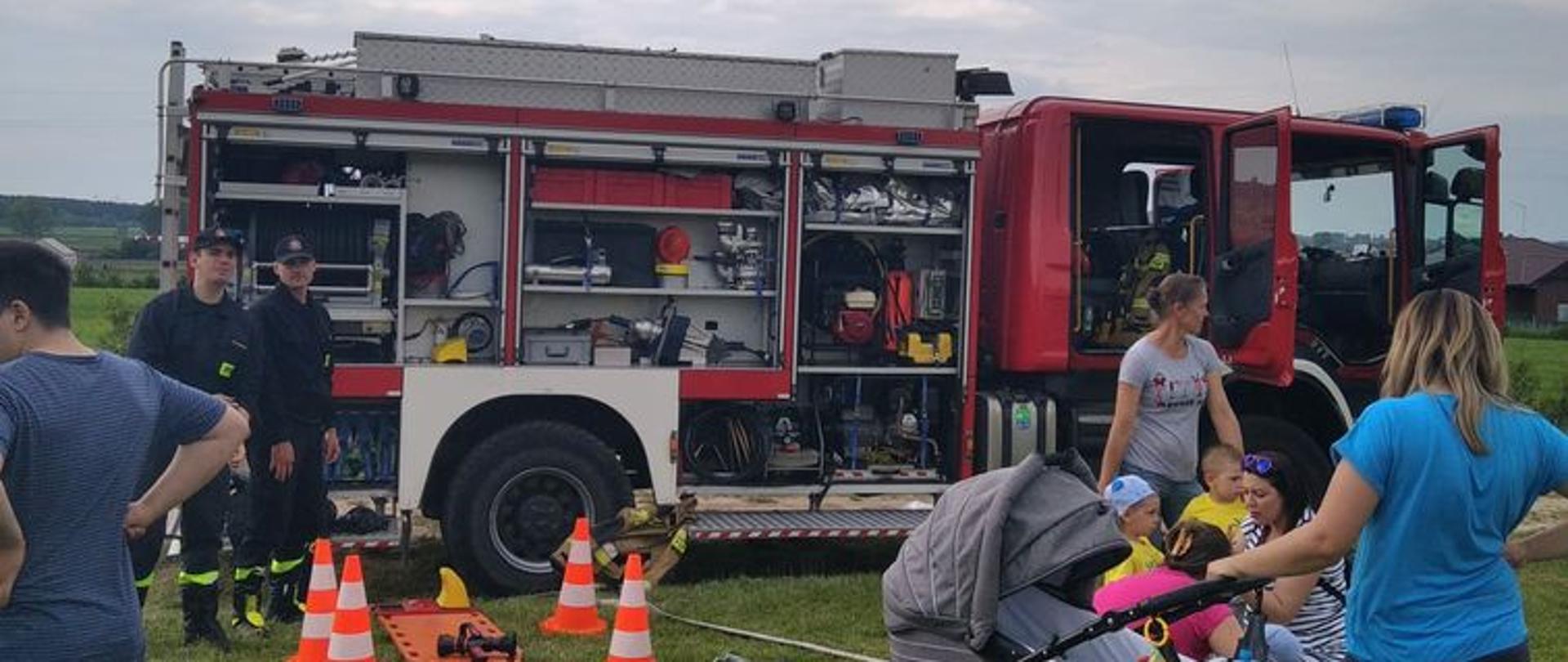 Zdjęcie przedstawia strażaków prezentujących dzieciom wóz strażacki SCANIA - GCBA 5/32/2,5.