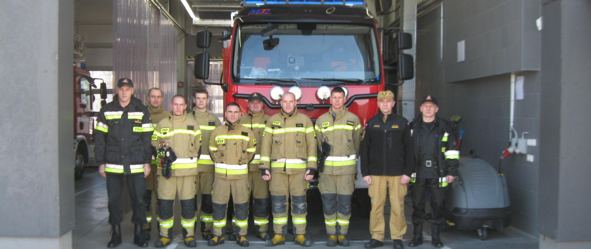 Strażacy komendy w Brzezinach zebrani przed samochodem pożarniczym