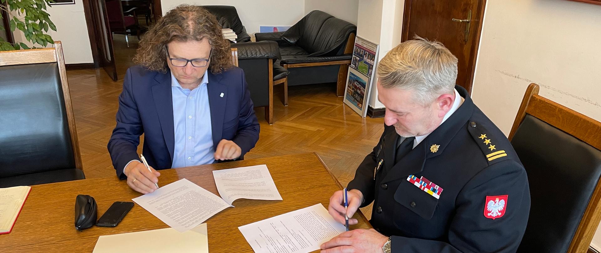Przy stole po prawej stronie siedzący w umundurowaniu wyjściowym Komendant Miejski a na wprost Prezyden Miasta pan Jacek Karnowski podpisuję porozumienie