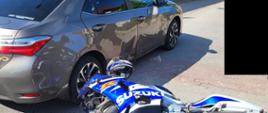 Widać uszkodzony prawy bok samochodu osobowego oraz leżący na drodze motocykl