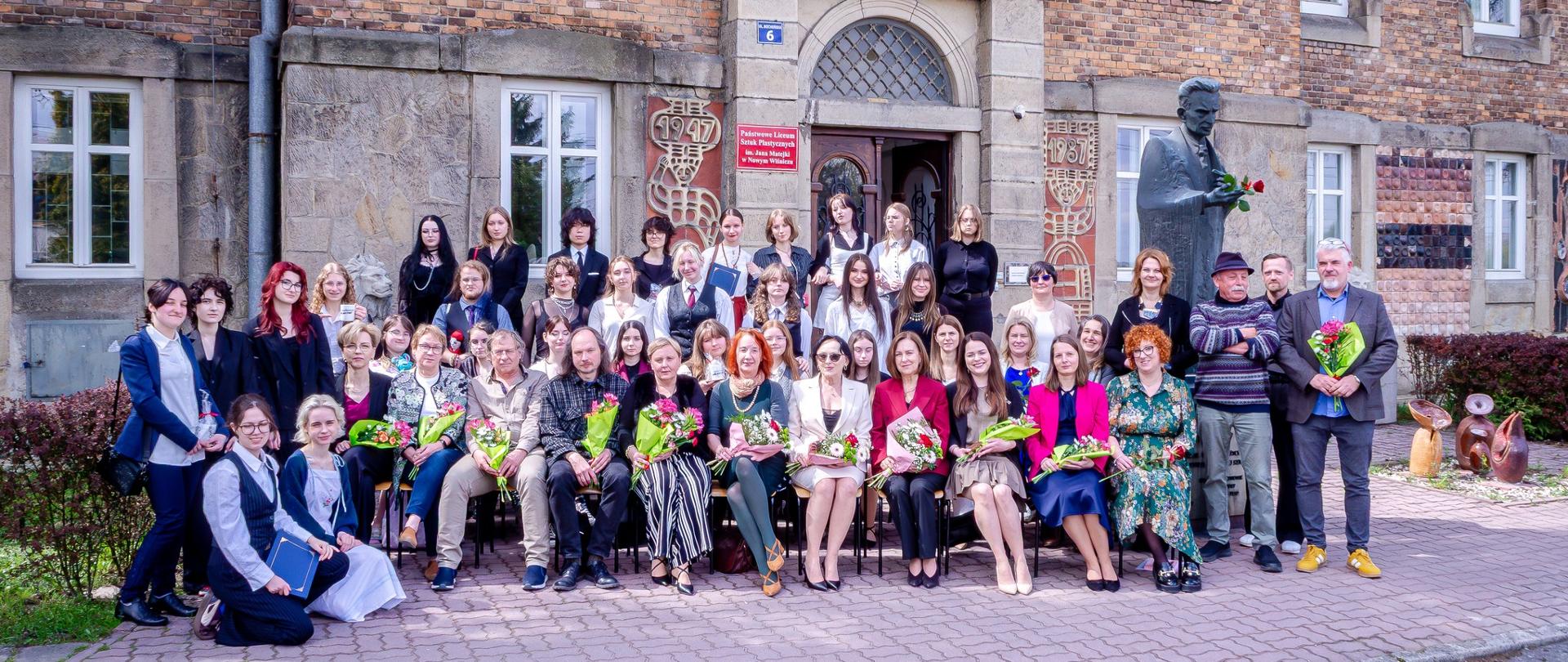 Zdjęcie przedstawia dużą grupę osób ustawionych do wspólnej fotografii przed budynkiem z czerwonej cegły.