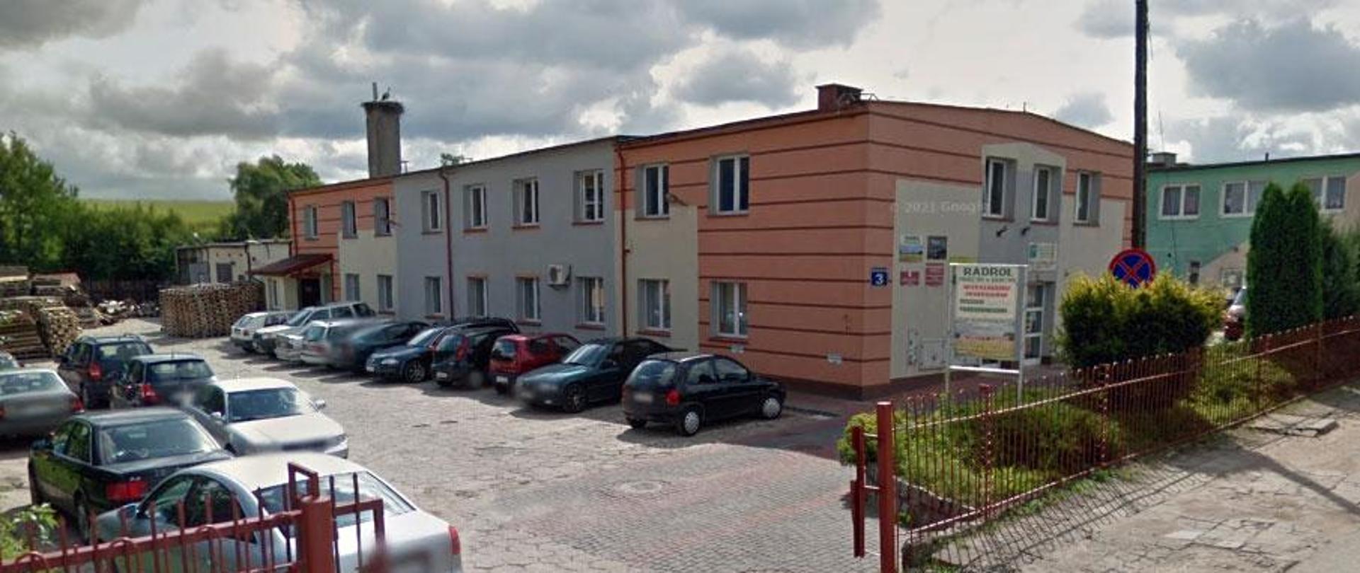 Dwupiętrowy budynek biurowy, otoczony parkingiem