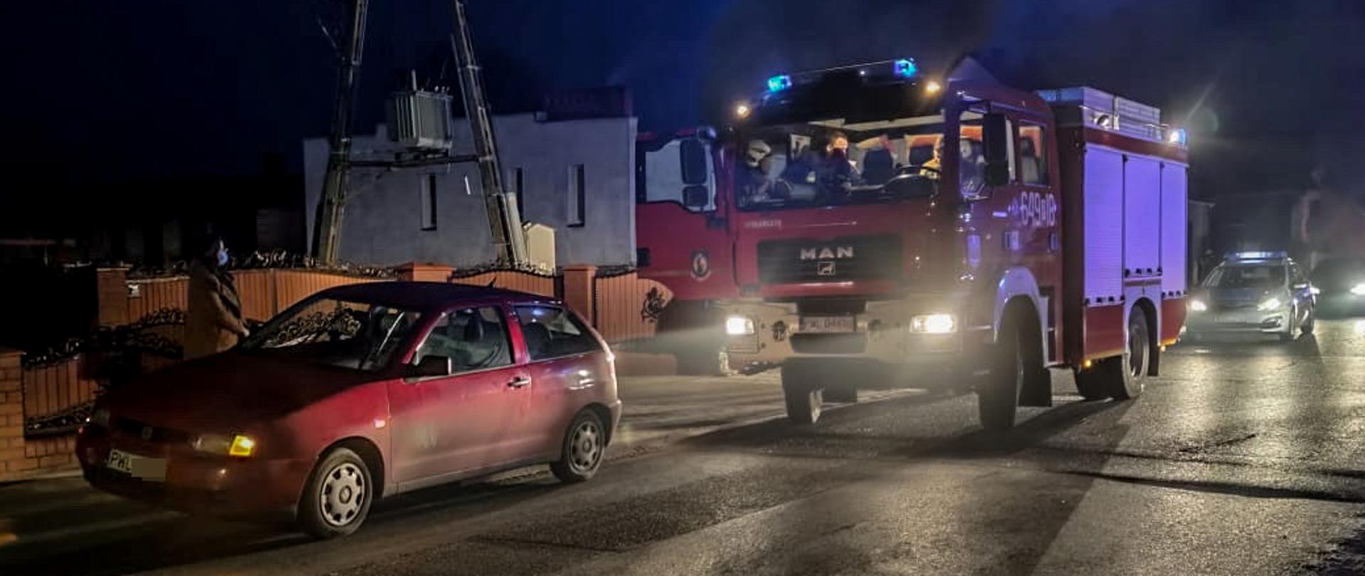 Noc, samochód osobowy, w tle samochód strażacki oraz radiowóz policyjny.