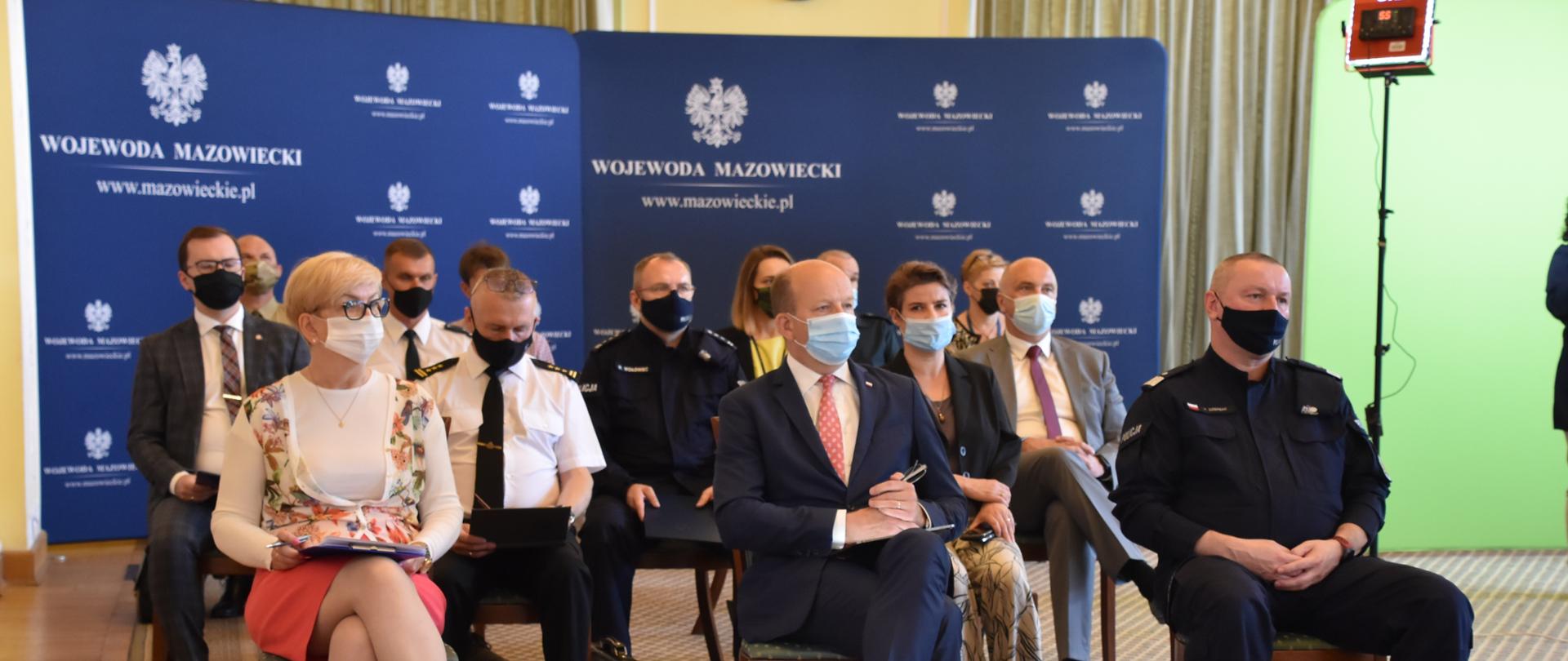 grupa mężczyzn i kobiet siedzi na krzesłach na konferencji prasowej poświęconej wakacjom 2021