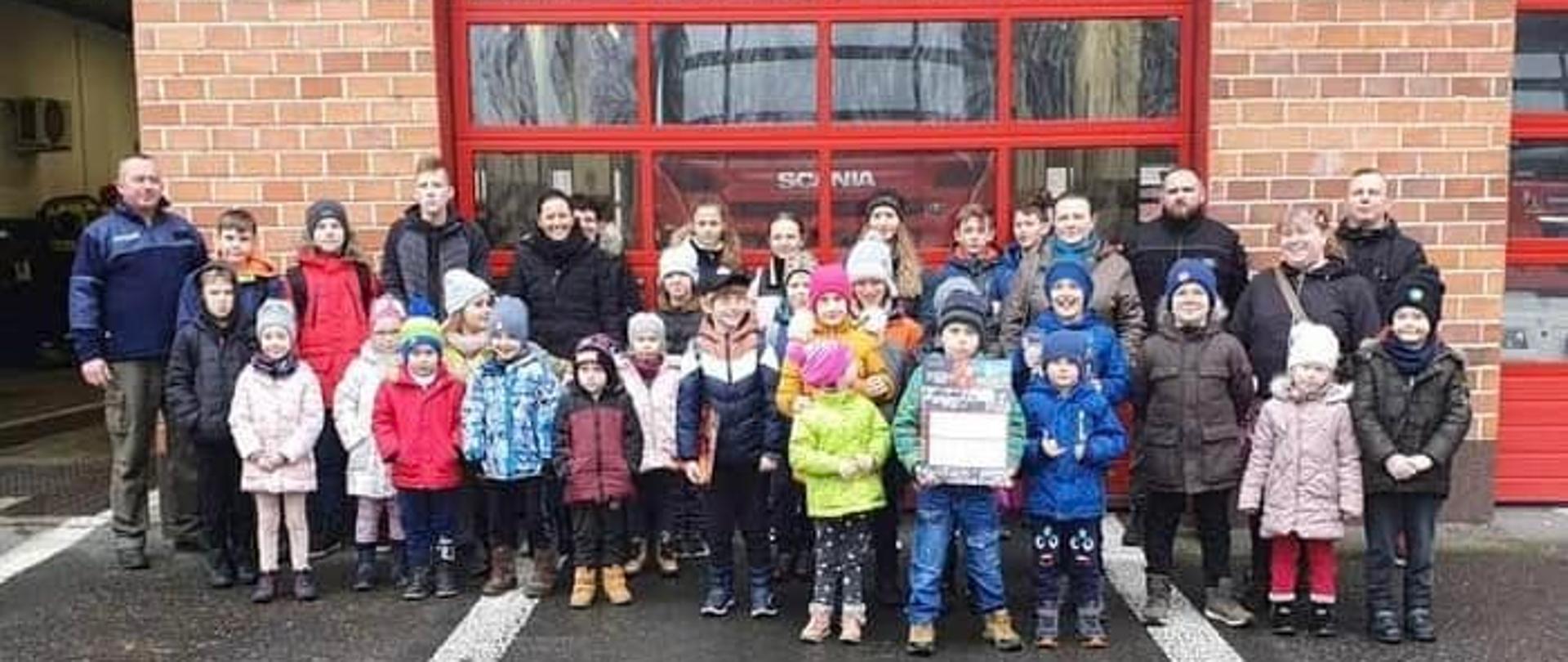 Na zdjęciu znajdują się dzieci oraz osoby dorosłe ustawione na tle bramy garażowej