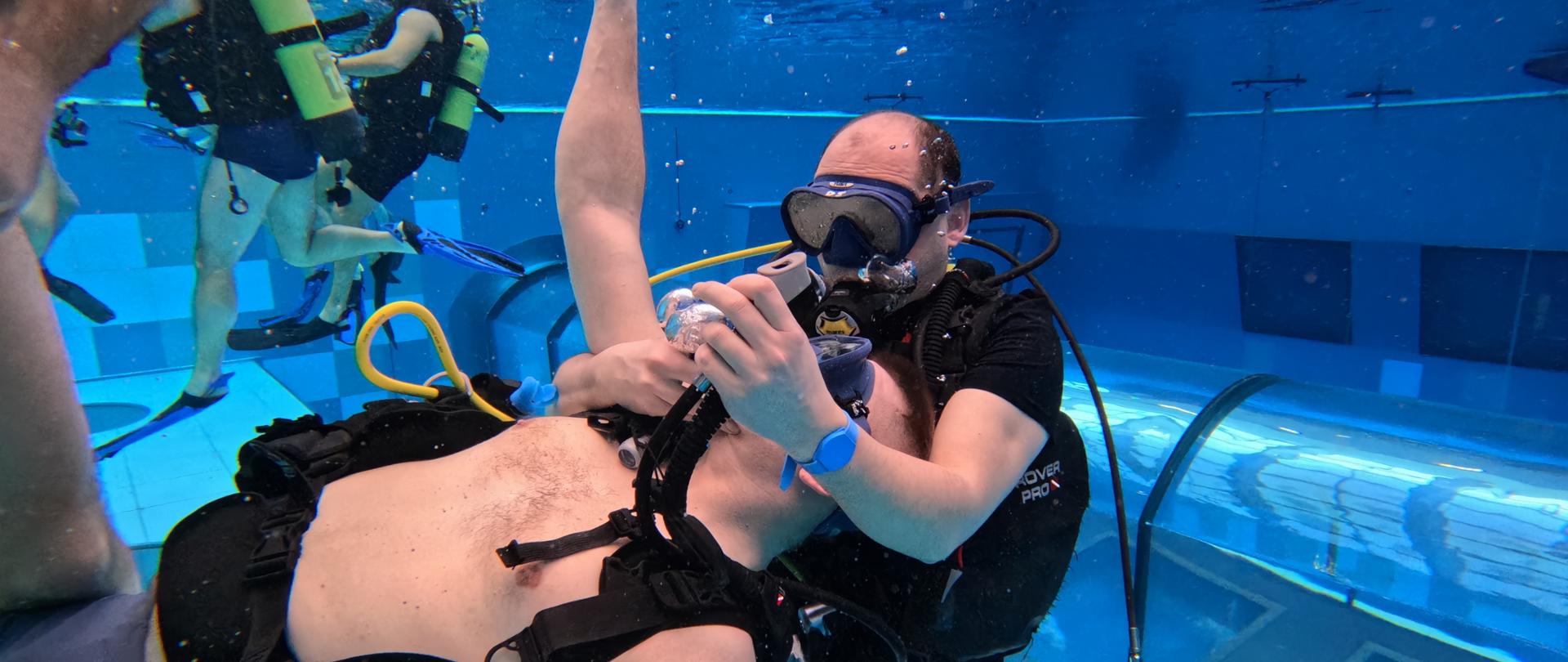 Strażacy ćwiczą pod wodą w parach ratowania nurka z wody, podczas symulowanego wypadku.