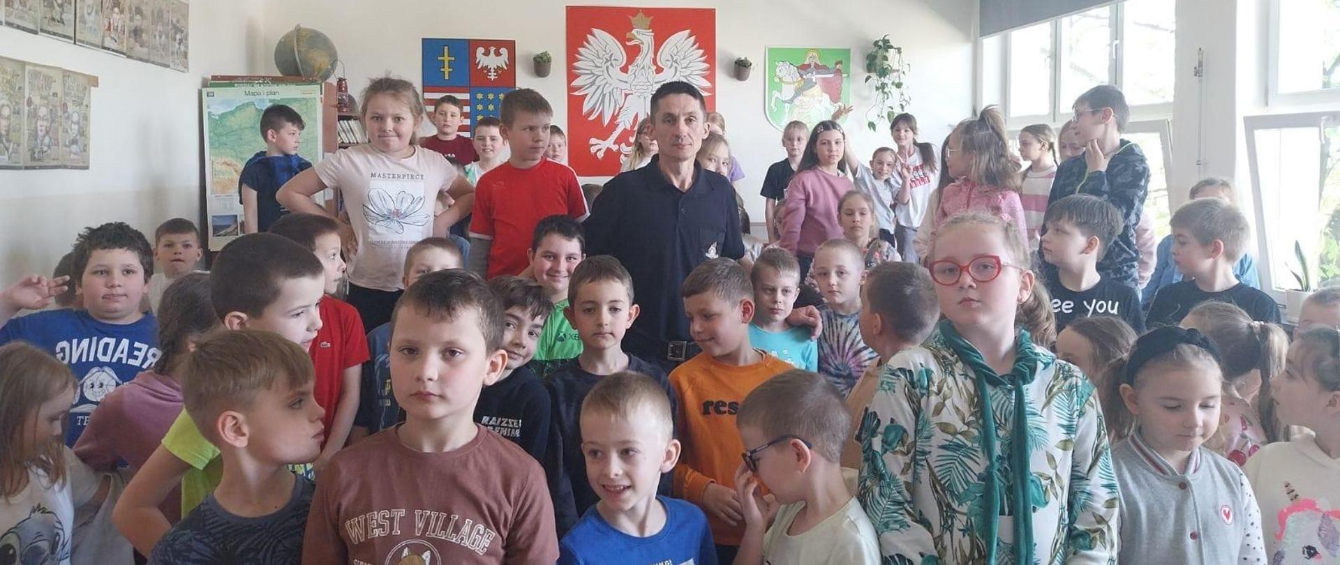 Zdjęcie grupowe dzieci i strażaka na tle godła polski