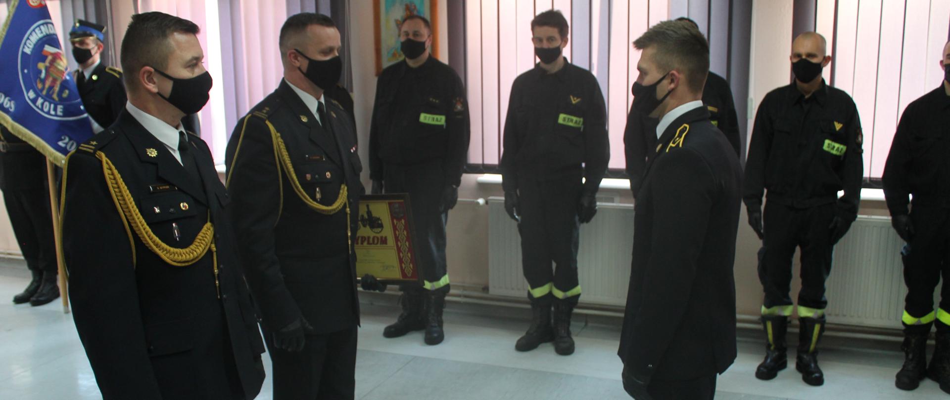 Zdjęcie przedstawia komendanta powiatowego PSP w Kole oraz zastępcę komendanta powiatowego PSP w Kole podczas wręczenia Dyplomu Komendanta Głównego mł. asp. Konradowi Siwińskiemu