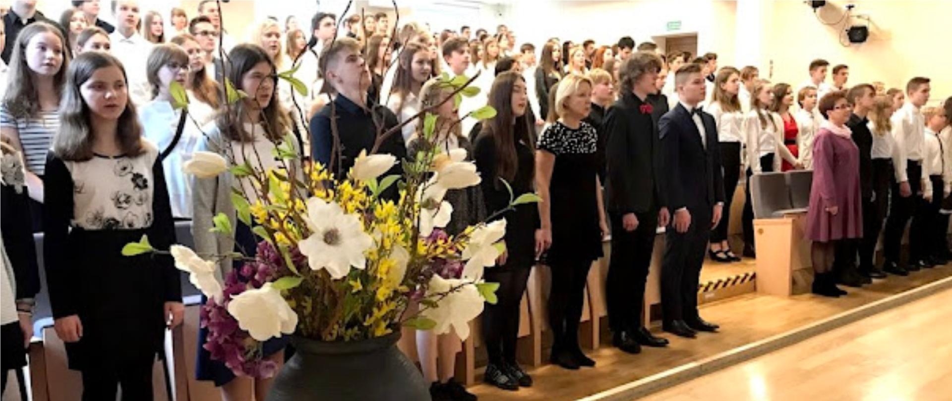 Grafika przedstawia uczniów ZPSM w Szczecienie, śpiewających Hymn Narodowy