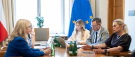 Minister Edukacji wraz z Minister Zdrowia i współpracownikami siedzą przy stole i rozmawiają.