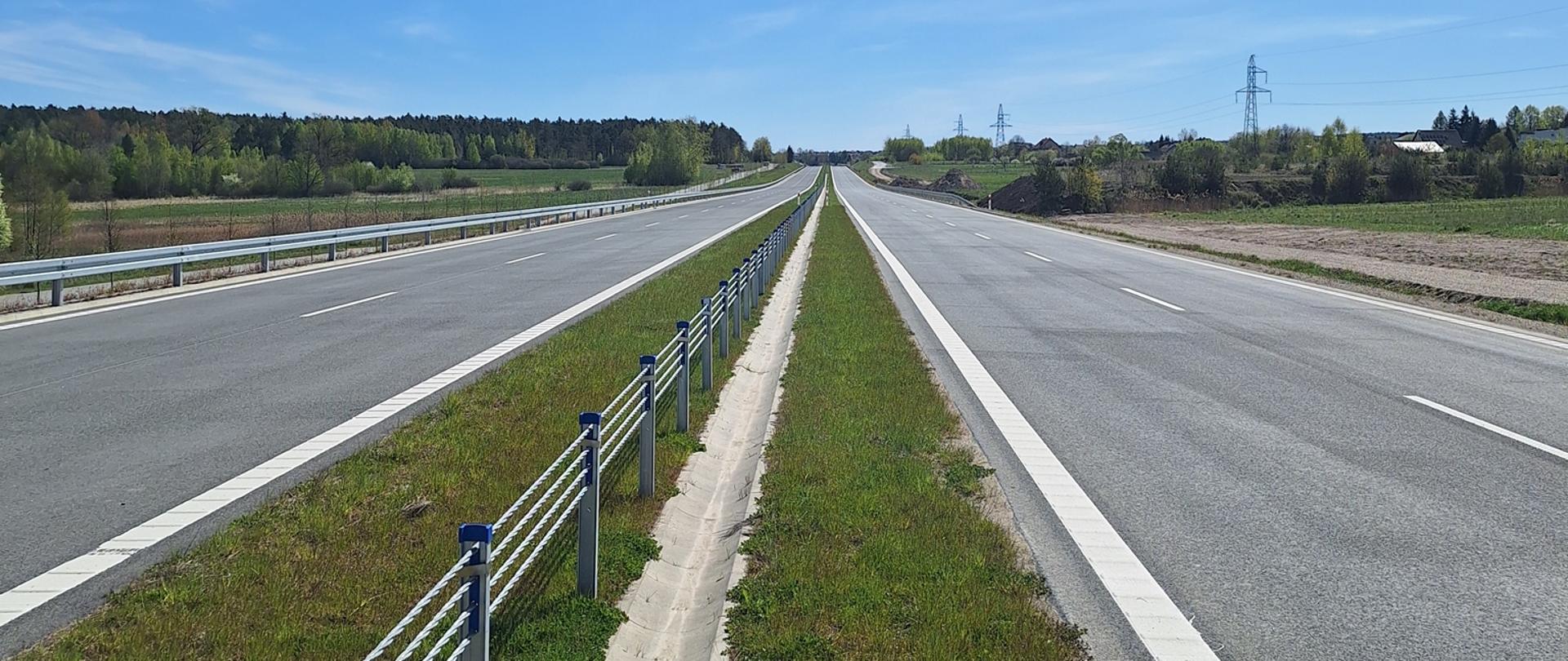 DK42 obwodnica Wąchocka - dwujezdniowa droga asfaltowa, po obu stronach zieleń, w oddali pojedyncze zabudowania