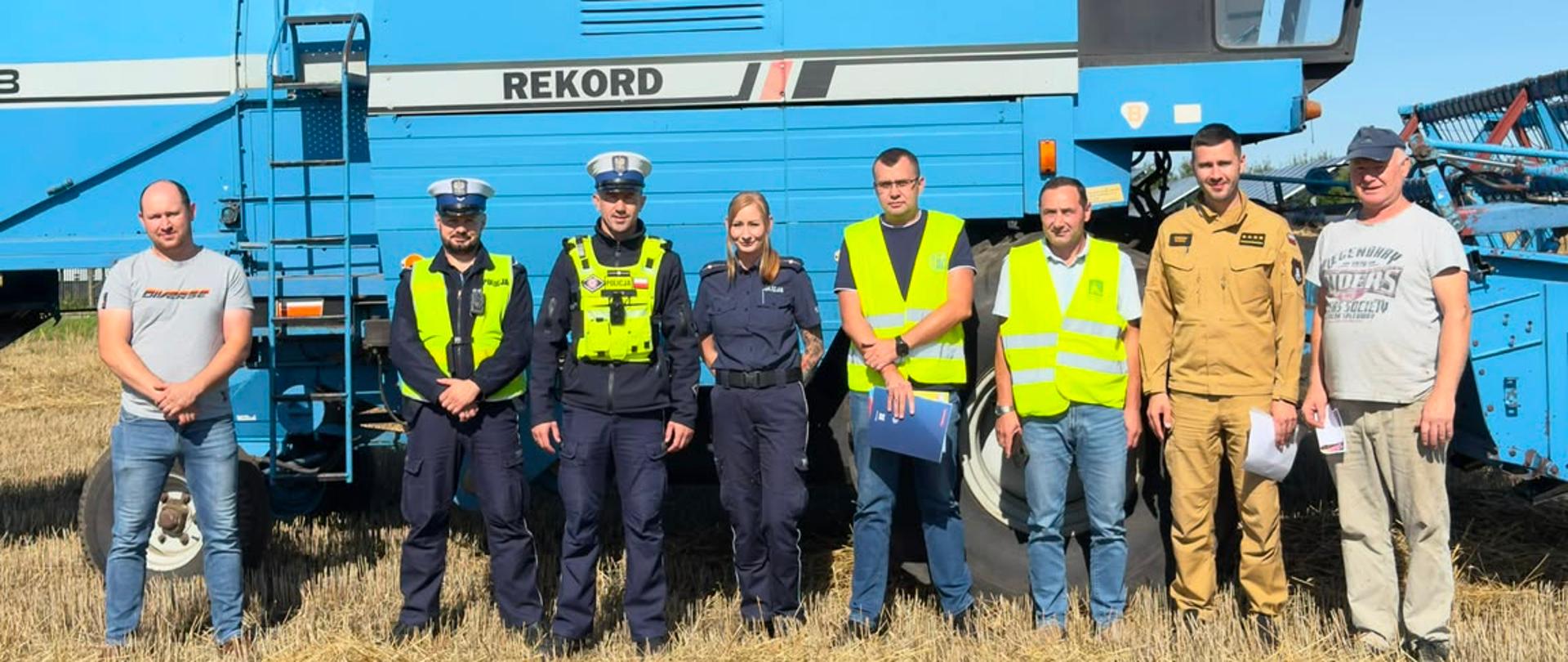 Działania prewencyjne podczas prac polowych. Strażak, policjanci oraz pracownicy Inspekcji Pracy i Kasy Rolniczego Ubezpieczenia Społecznego wraz z rolnikiem stoją na polu przed kombajnem. 