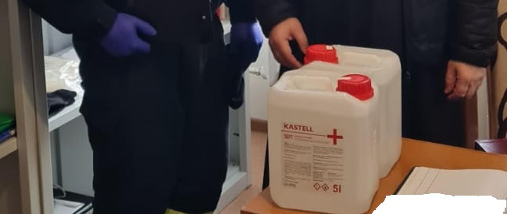 Zdjęcie obrazuje przekazanie księdzu przez strażaka płynu do dezynfekcji.
