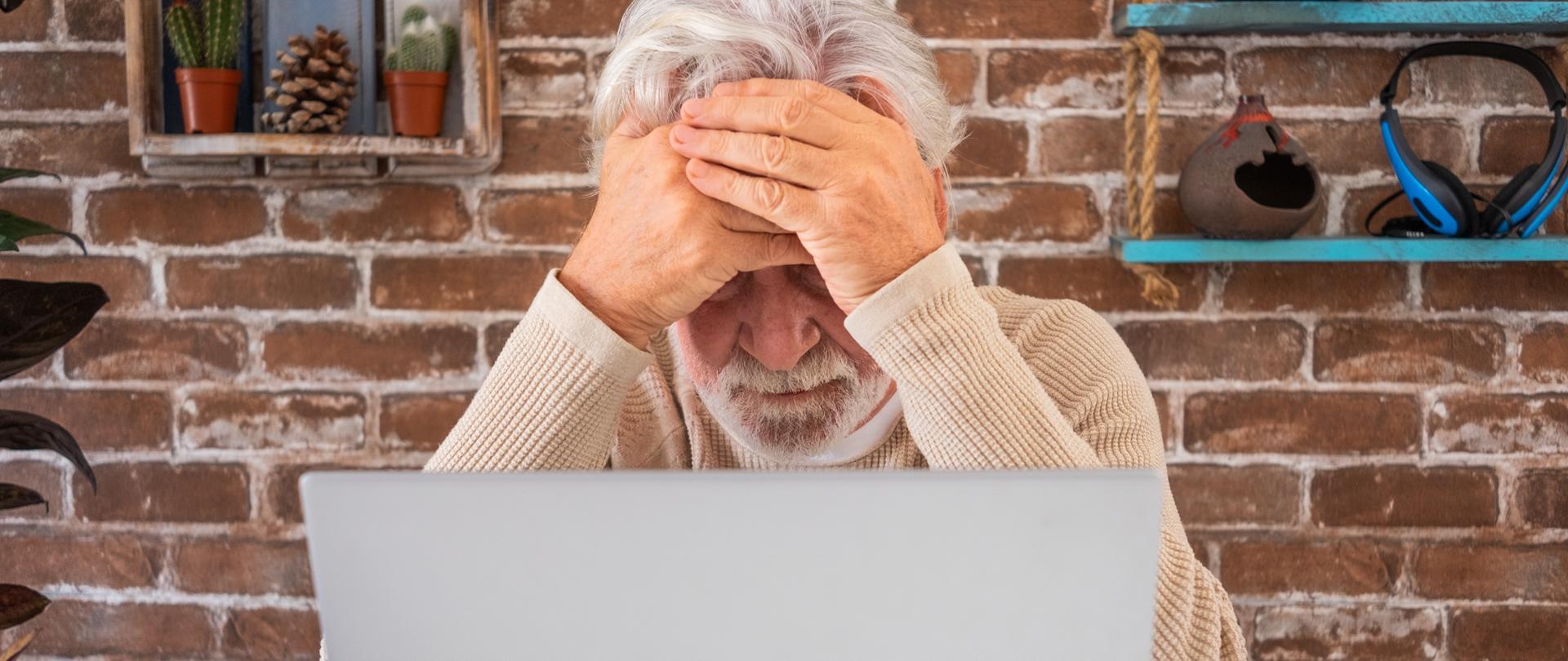 starszy mężczyzna siedzi przed laptopem i załamuje ręce jakby sobie nie radził z komputerem