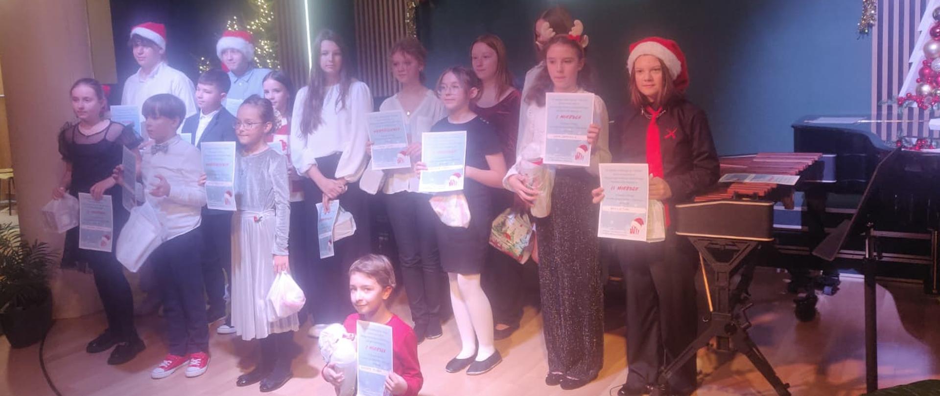 Na zdjęciu widać dzieci trzymające w rękach dyplomy za uczestnictwo w konkursie w tle widoczna jest Zielona ściana z logo szkoły