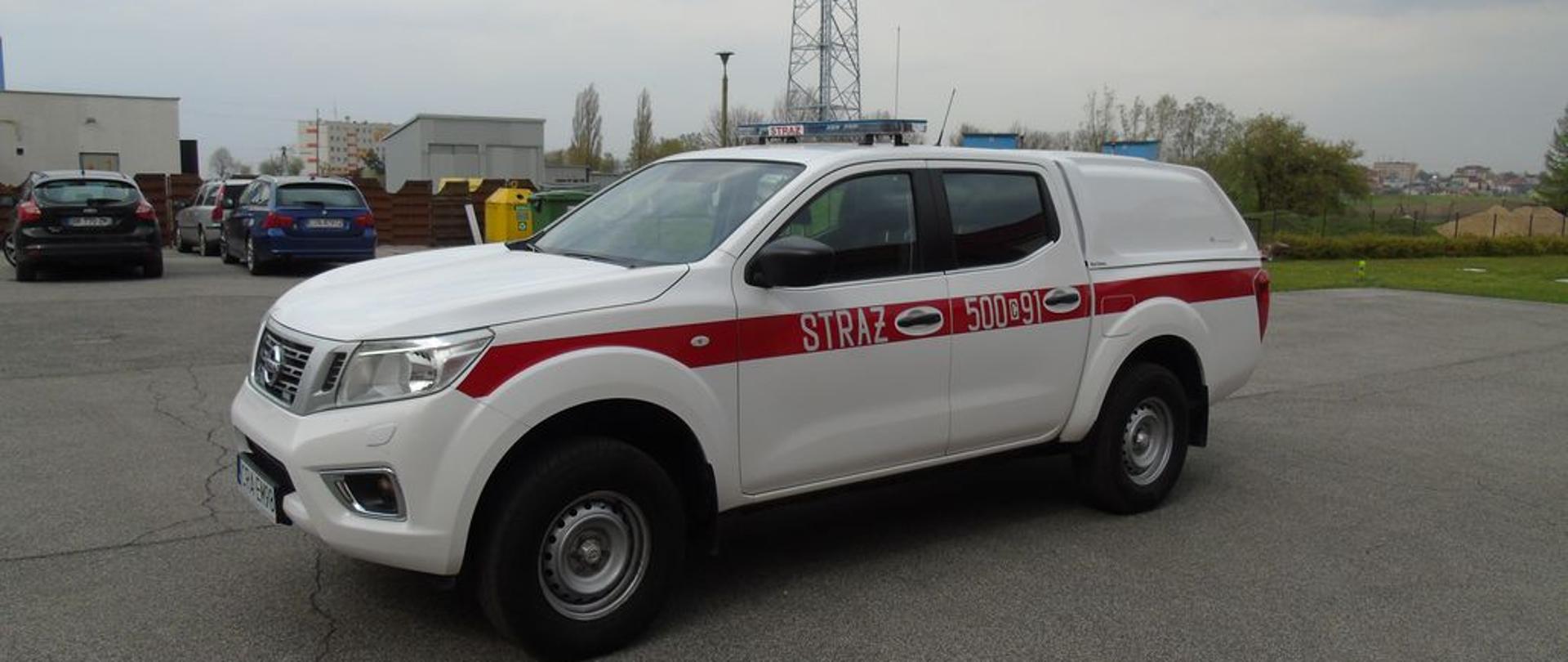 Zdjęcie przedstawia biały samochód SLOP Nissan Navara na tle placu manewrowego KP PSP.