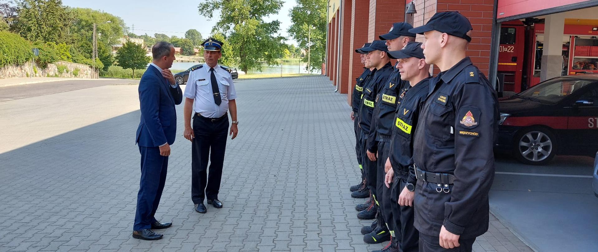 Na zdjęciu widzimy komendanta KP PSP Międzychód oraz Wojewodę Wielkopolskiego. W tle strażaków, oraz garaże PSP.