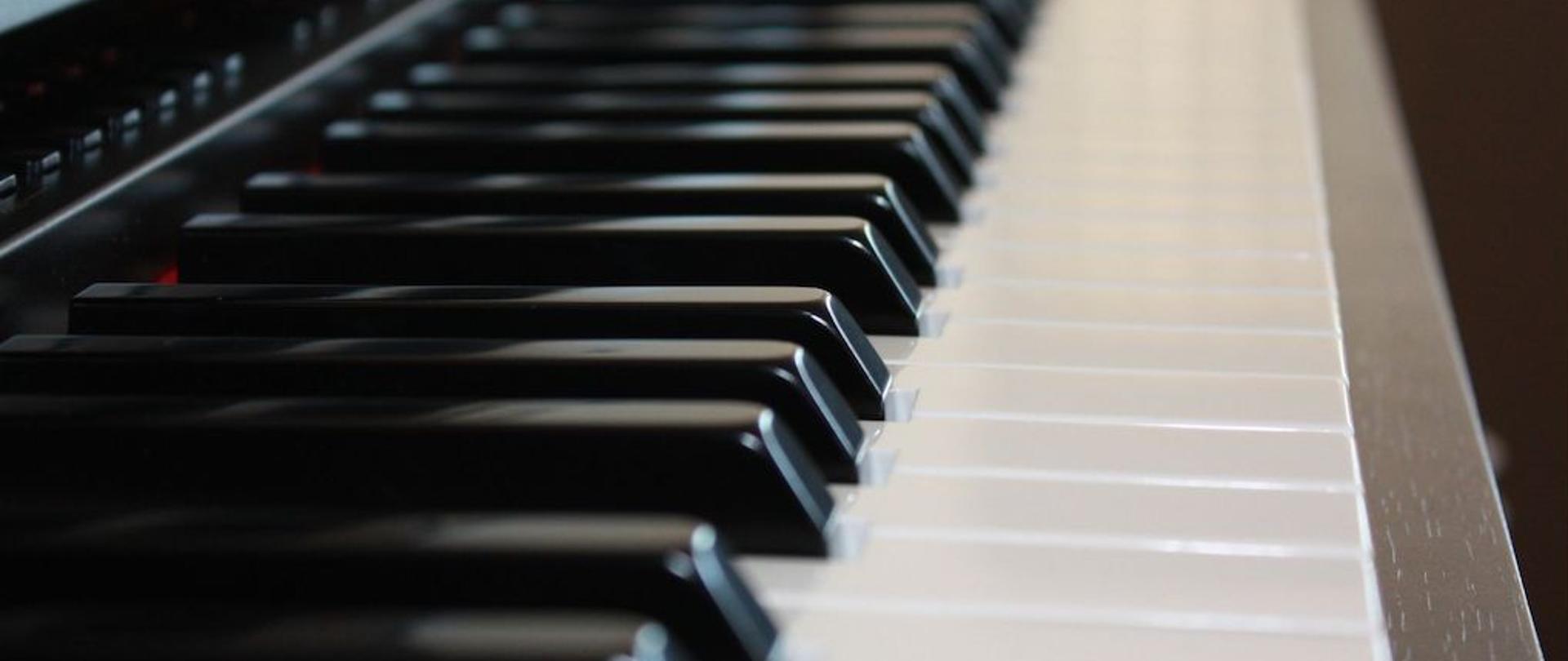 Zdjęcie klawiatury fortepianu z boku z lewej strony. Kolorystyka czarno biała.