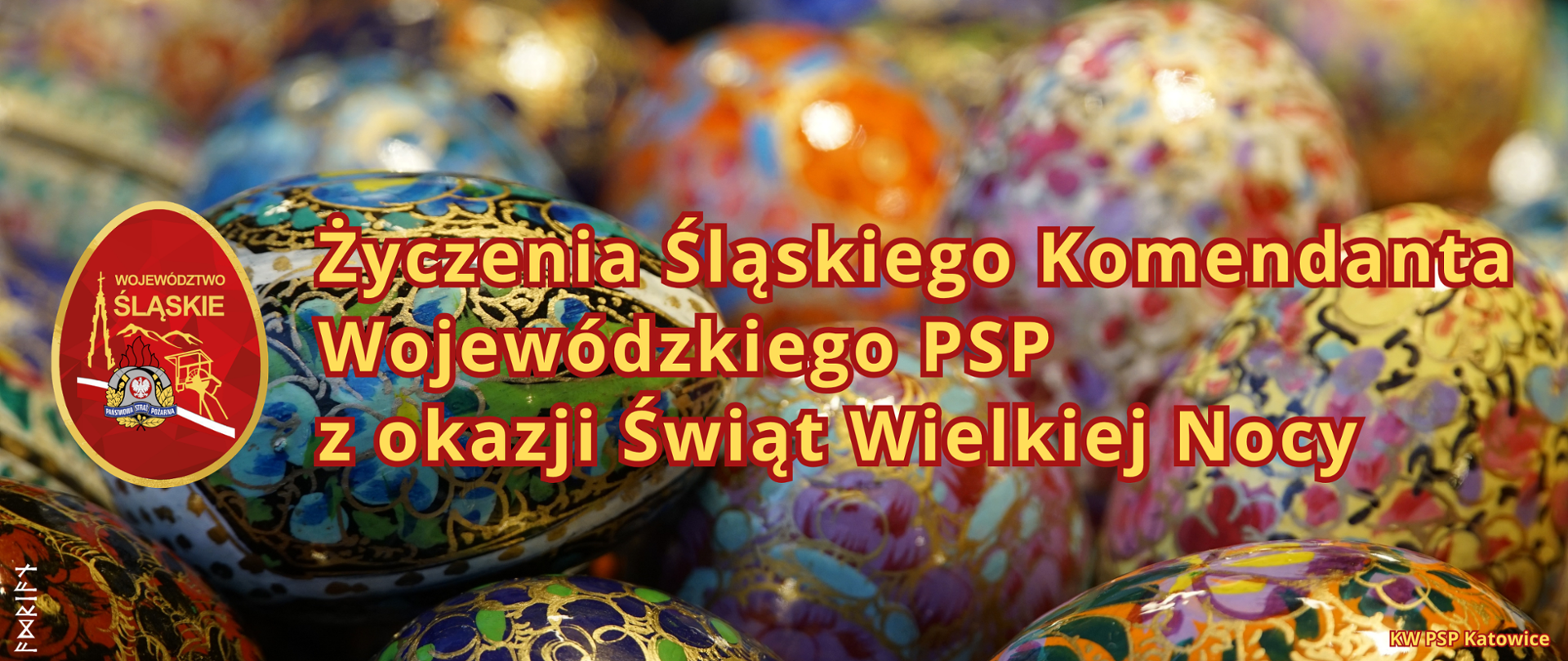 Grafika to świąteczna karta z życzeniami. Całą przestrzeń wypełniają kolorowe, bogato zdobione pisanki. Jajka mają misterne wzory (kwiatowe i geometryczne) w odcieniach błękitu, złota, czerwieni i fioletu. W centralnej części znajduje się duży, czytelny napis w kolorze żółtym z ciemniejszą obwódką: „Życzenia Śląskiego Komendanta Wojewódzkiego PSP z okazji Świąt Wielkiej Nocy” Po lewej stronie widnieje okrągłe logo PSP województwa śląskiego. W prawym dolnym rogu znajduje się mniejszy napis: „KW PSP Katowice” (Komenda Wojewódzka Państwowej Straży Pożarnej).