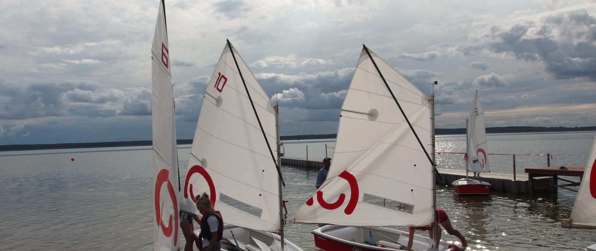 Cztery łódki typu optimist z żaglami z logo Polska pomoc na wodzie
