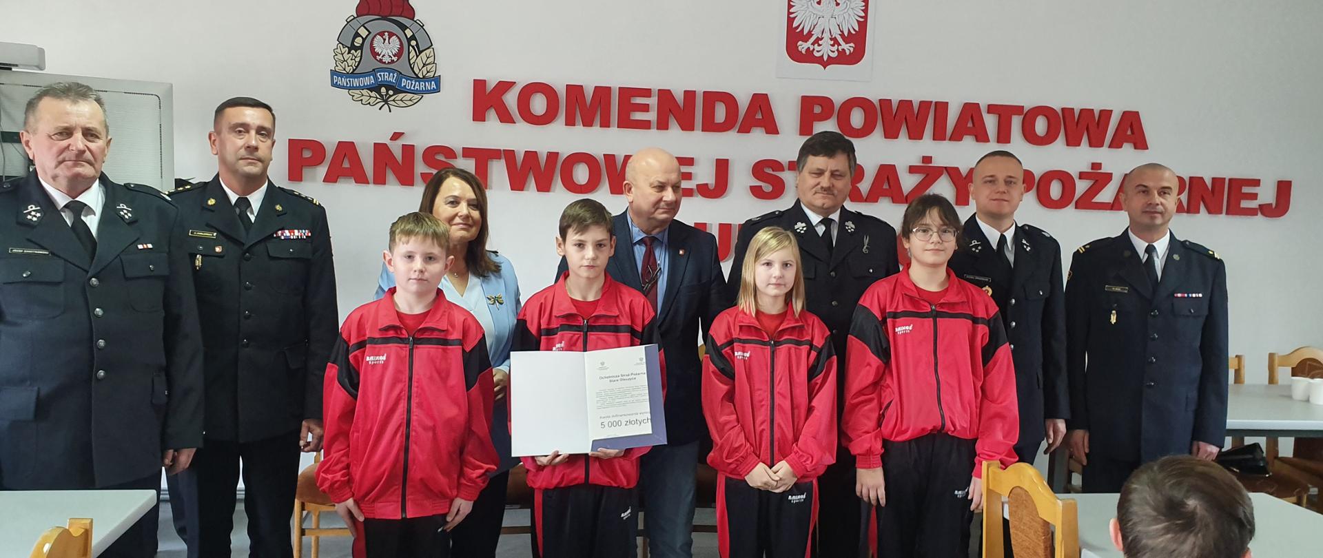 Zdjęcie przedstawia Zastępcę Podkarpackiego Komendanta Wojewódzkiego w Rzeszowie, st. bryg. Janusza Jabłońskiego, Panią Poseł na Sejm RP Teresę Pamułe, Starostę Powiatu lubaczowskiego pana Zenona Swatka oraz Komendanta Powiatowego PSP w Lubaczowie mł. bryg. Wojecha Wusa wraz z osobami które otrzymały Promesy