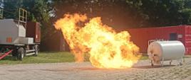 Zbiornik ćwiczebny LPG stojący na szkolnym poligonie, obok po lewej widoczny słup ognia