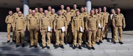 Pamiątkowe zdjęcie grupowe funkcjonariuszy PSP będących uczestnikami szkolenia z zakresu kierowania działaniem ratowniczym na poziomie interwencyjnym (20 osób) w towarzystwie Zastępcy Komendanta CS PSP, kobiety oraz dwóch funkcjonariuszy CS PSP